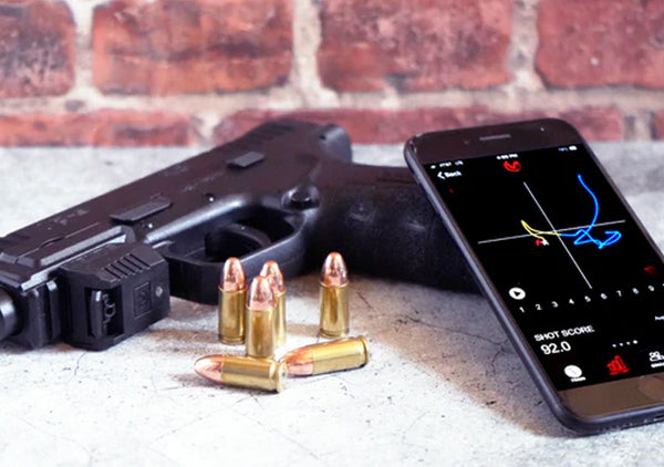 Pistol on Side with Mantis X10 Mounted, Phone Leaning on Gun and Ammo on Table